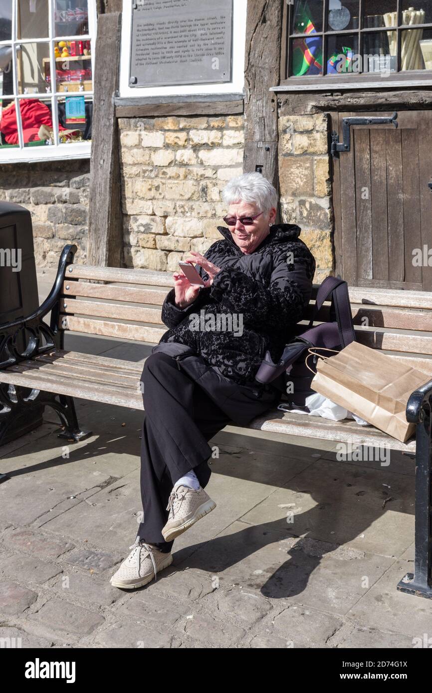 Lächelnde ältere Frau, die im Freien nach Mobiltelefonen schaut, Großbritannien Stockfoto
