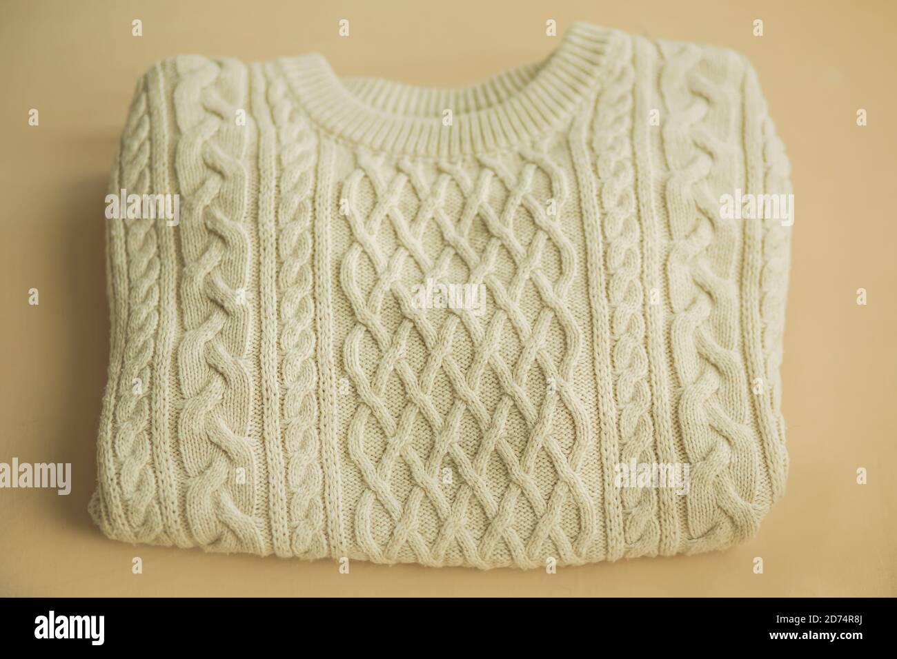 Draufsicht auf einen hübsch gefalteten warmweißen Strickpullover aus Wolle mit Mustern, der auf beigem Hintergrund liegt. Kleidung für kaltes Wetter. Stockfoto