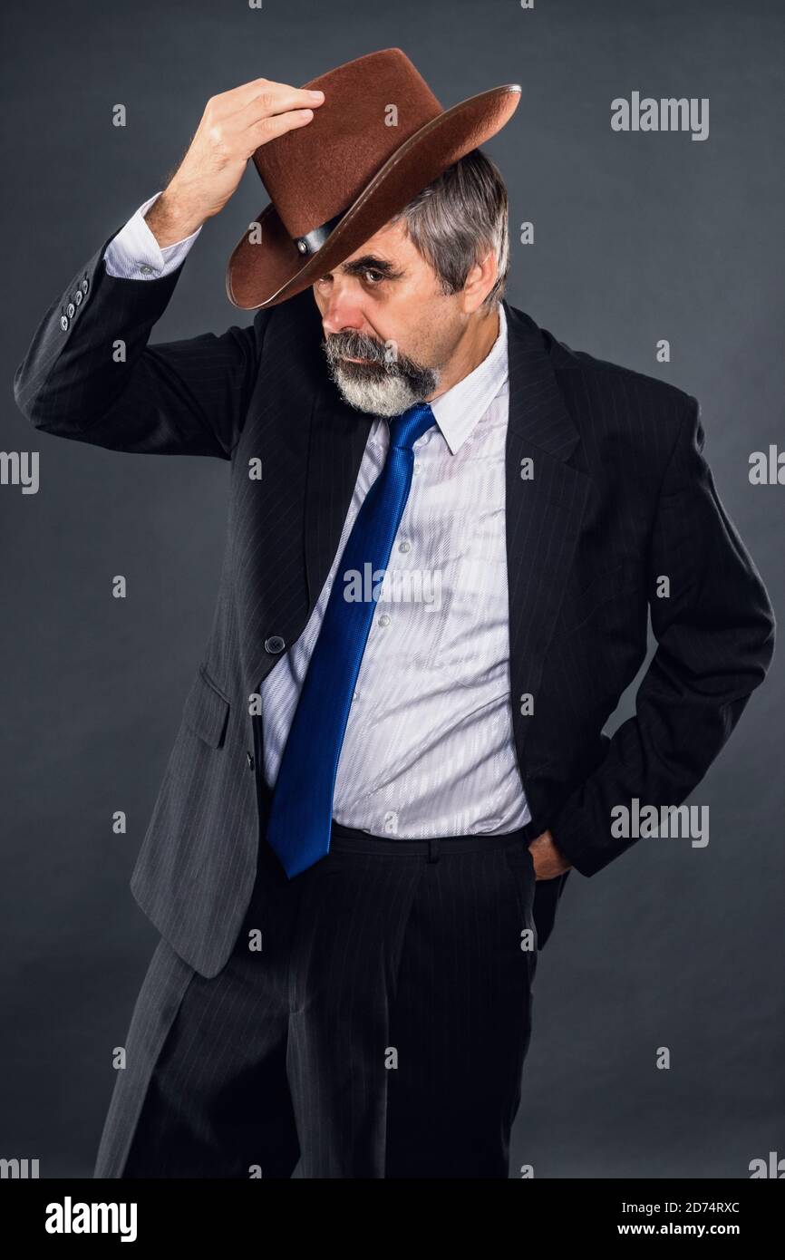 Älterer expressiver Dandy-Mann in einem Anzug mit Krawatte Bows Auf Wiedersehen schön und setzt auf einen Hut Stockfoto