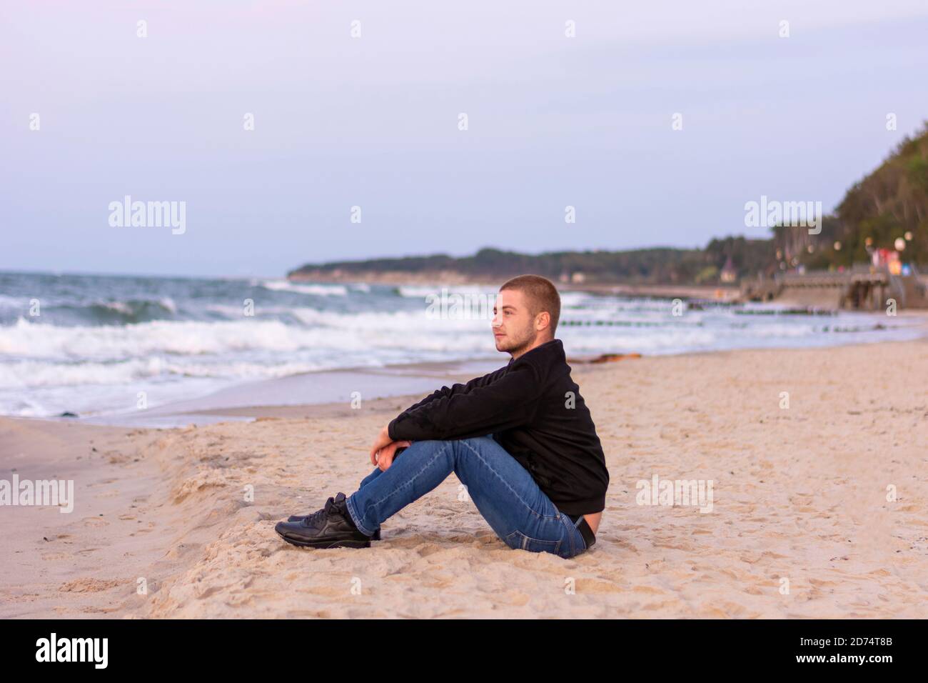 Ein junger gutaussehender Mann mit Bart ruht am Abend bei Sonnenuntergang am Meer. Romantische Stimmung, selektiver Fokus. Stockfoto