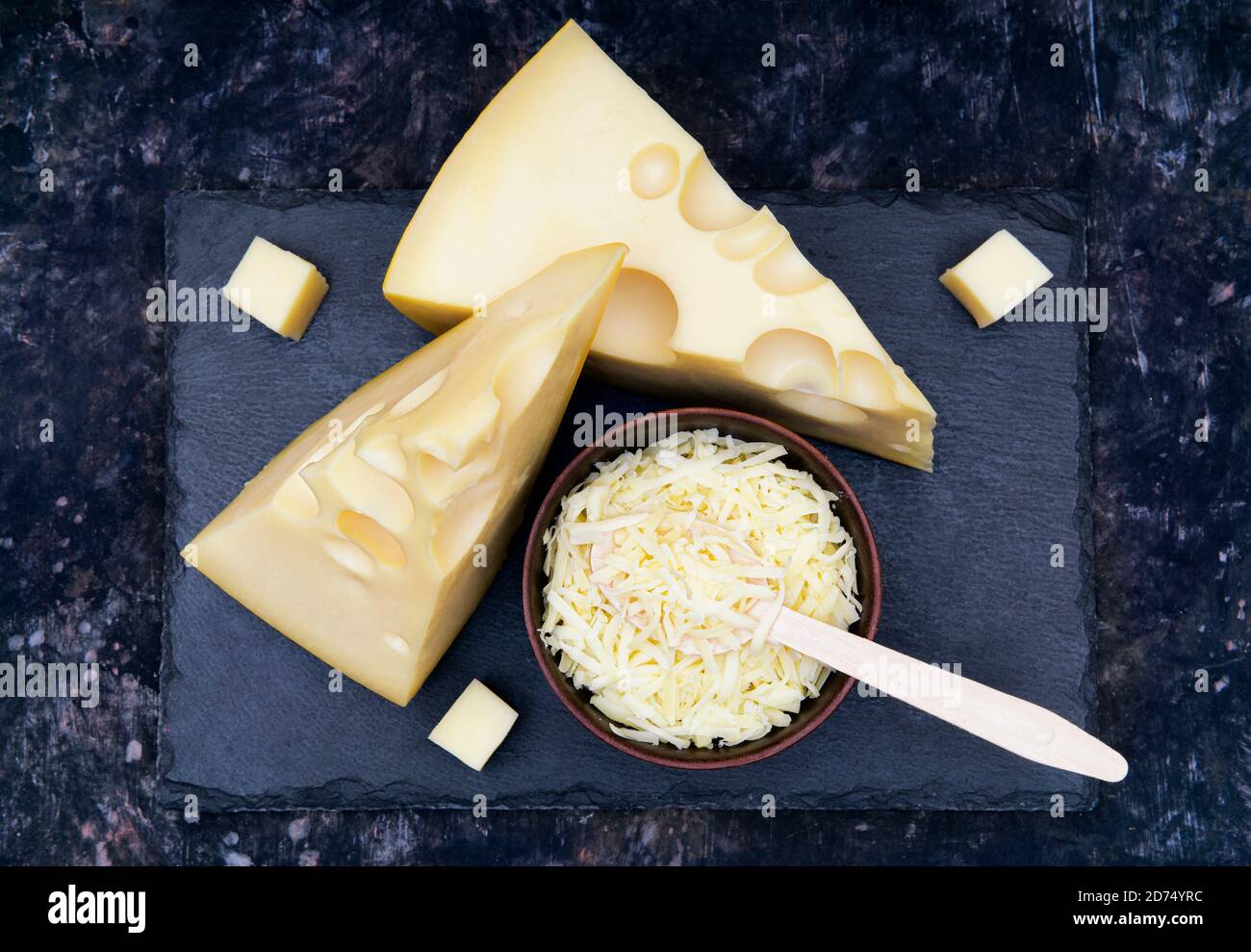 Zwei Käsekeile und eine Schüssel mit geriebenem Käse Ein schwarzes Steinbrett Stockfoto