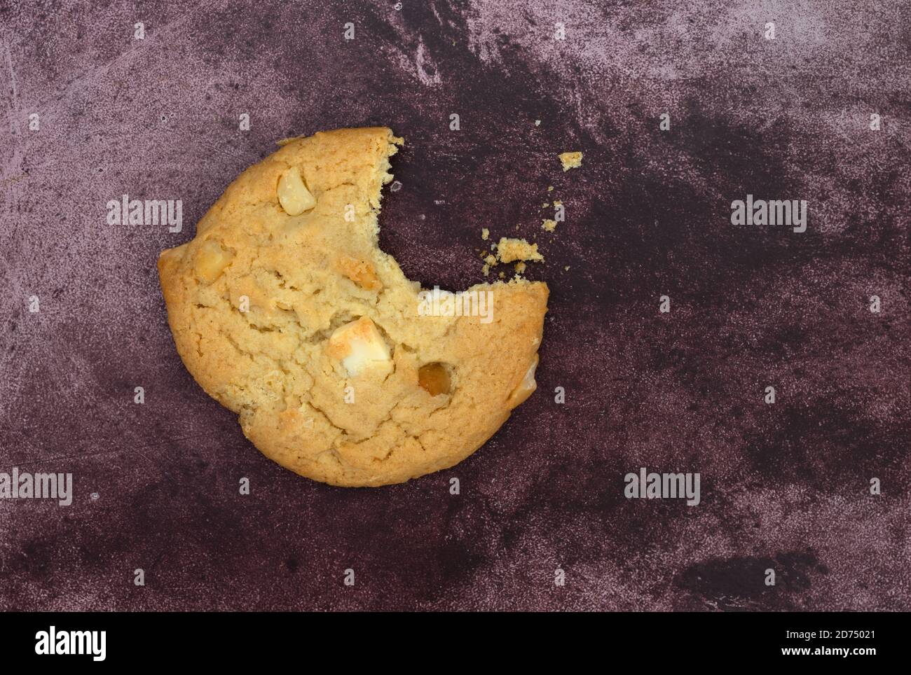 Gourmet Macadamia Nuss und weiße Schokolade Cookie fehlt ein Biss mit Krümel auf einem kastanienbraunen Hintergrund. Stockfoto