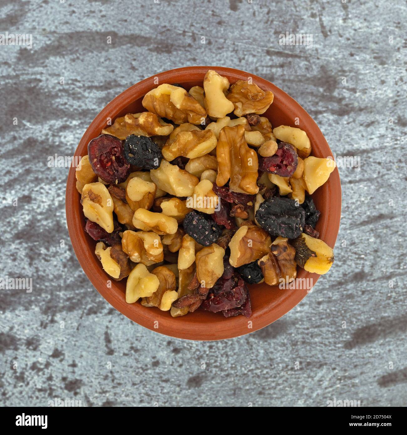 Draufsicht auf eine Portion Nüsse und getrocknete Früchte Trail Mix in einer kleinen Tonschale auf grauem Hintergrund. Stockfoto