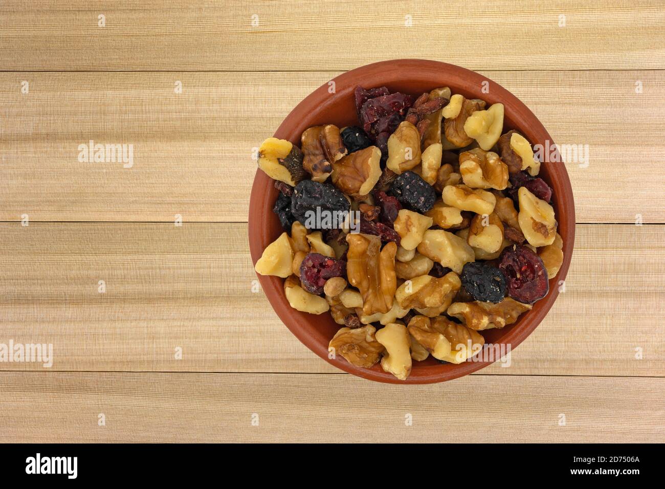 Draufsicht auf eine Portion Nüsse und getrocknete Früchte Trail Mix in einer kleinen Tonschale auf einem Zedernholz Hintergrund. Stockfoto
