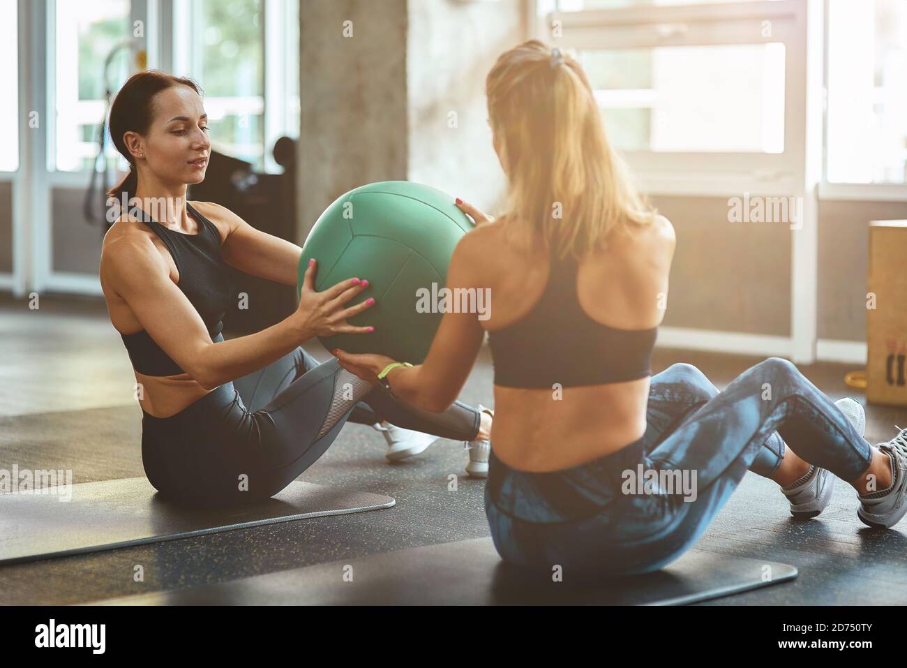 Gemeinsam arbeiten. Zwei junge sportliche Frauen in Sportbekleidung trainieren mit Ball im Fitnessstudio. Sport, Training, Wellness und gesunder Lebensstil Stockfoto