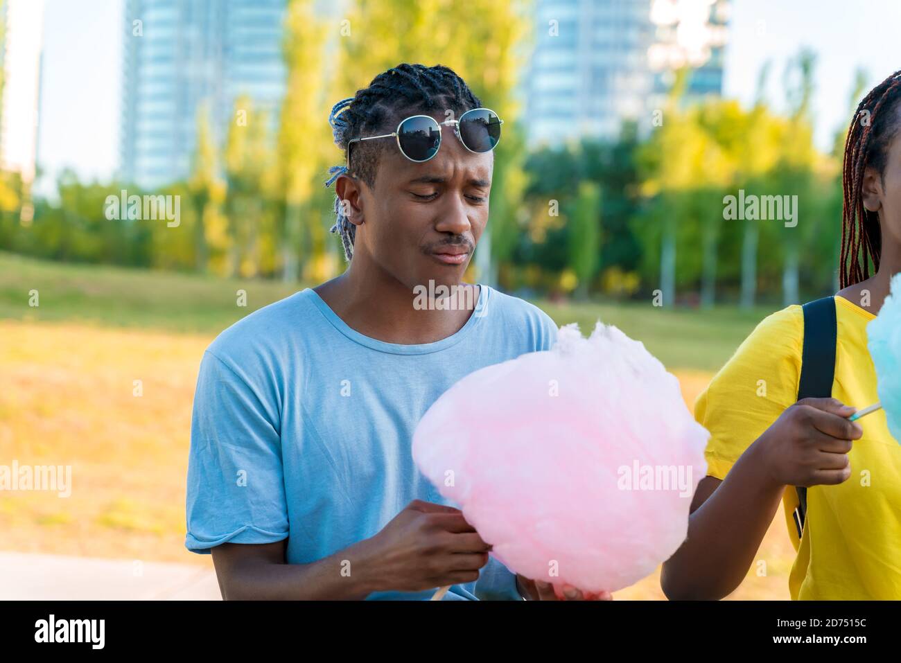 Ein glückliches schwarzes Paar, das bunte Zuckerwatte zusammen in einem Park einer großen Stadt hat. Stockfoto