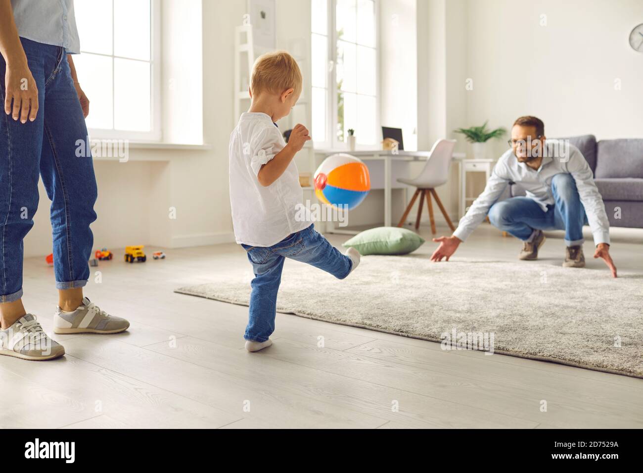 Fröhlicher junger Vater, Mama und kleiner Sohn, der mit aufblasbarem Ball im gemütlichen Wohnzimmer Fußball spielt Stockfoto