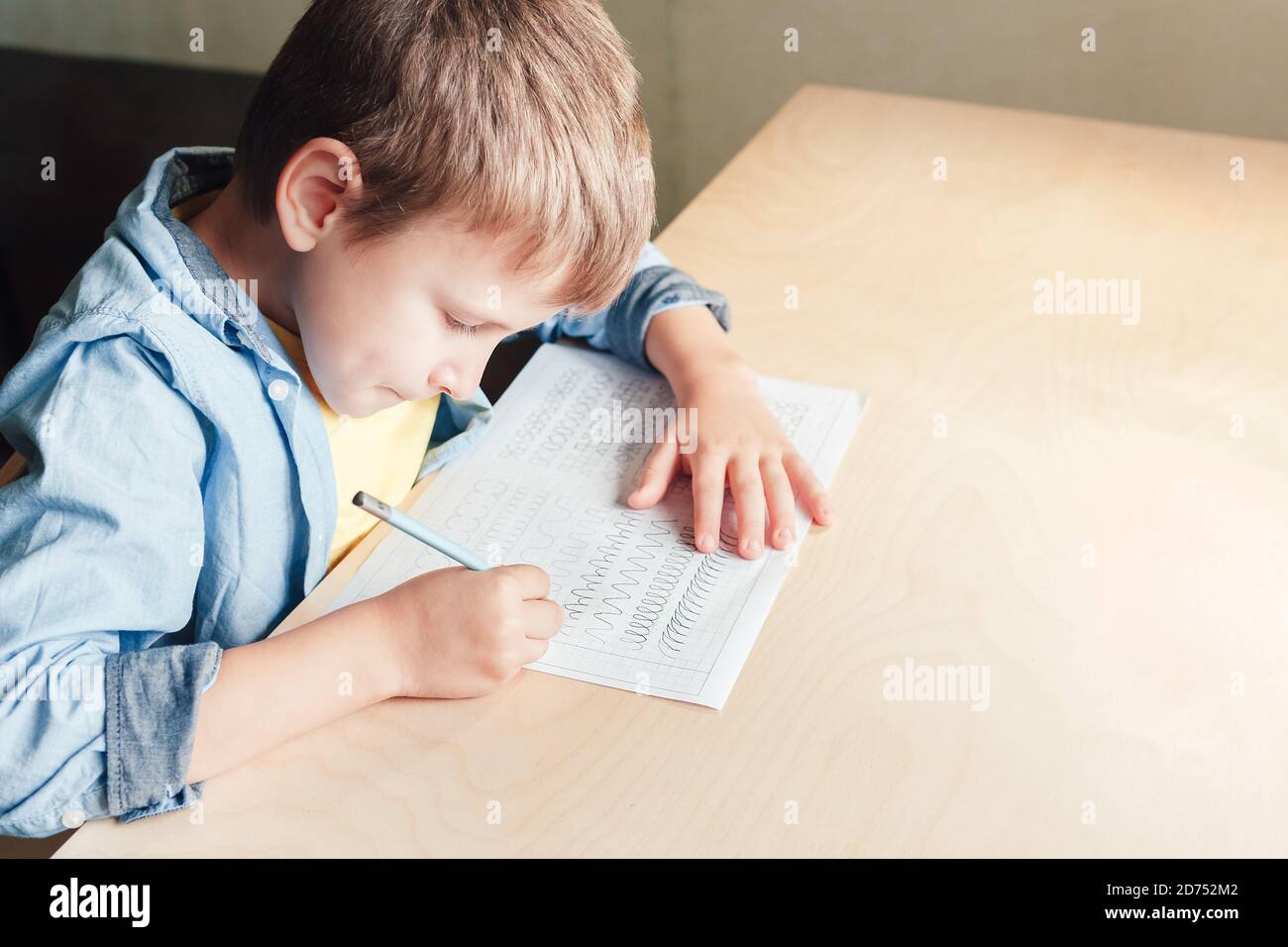 Nahaufnahme von niedlichen Jungen tun seine Hausaufgaben. Kind verschiedene Linien mit Bleistift schreiben. Konzept der Kindererziehung. Stockfoto