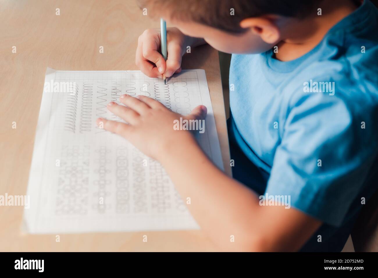 Nahaufnahme von niedlichen Kind tun seine Hausaufgaben. Kind verschiedene Linien mit Bleistift schreiben. Konzept der Kindererziehung. Stockfoto