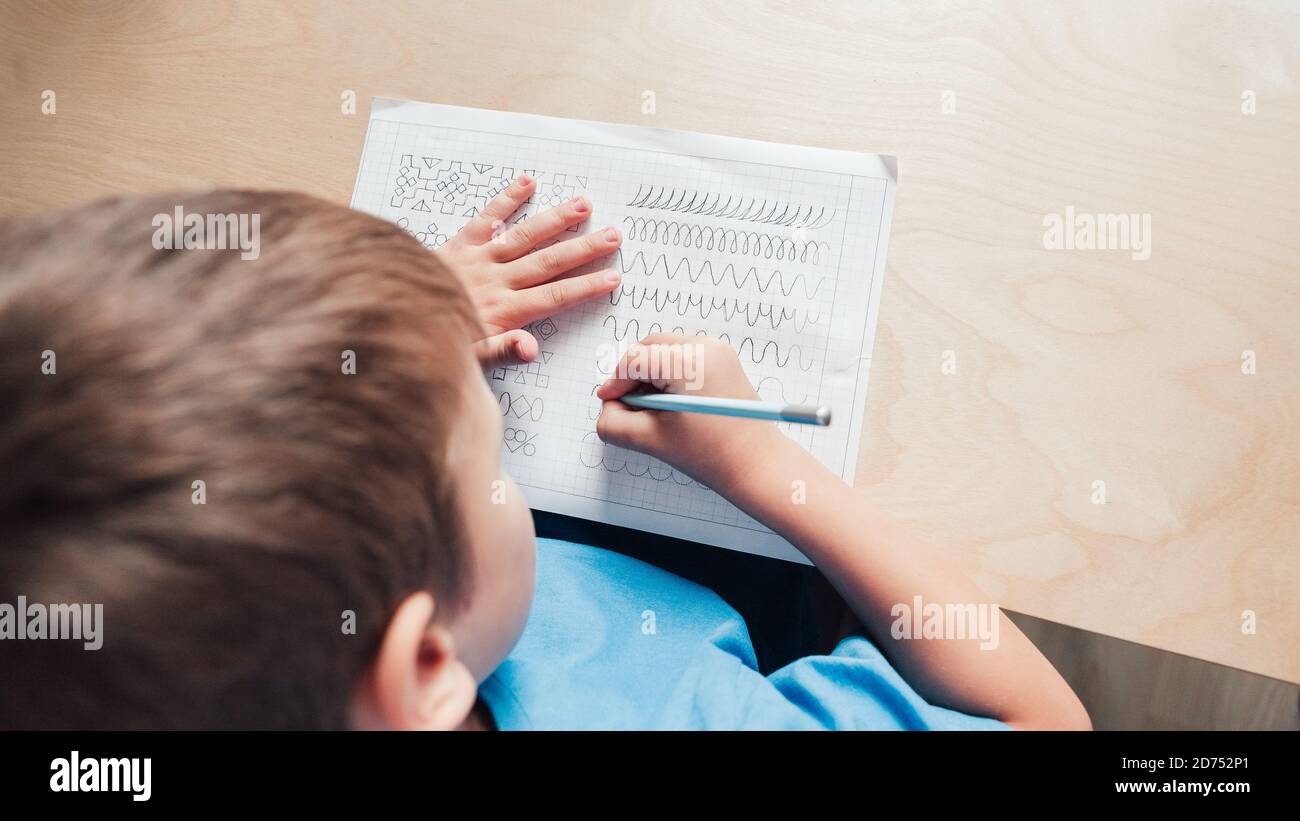 Kind Junge schreiben verschiedene Linien mit Bleistift. Vorschreiben Übung, um die Hände für das Schreiben von Briefen vorzubereiten. Konzept der Kindererziehung. Blick von oben Stockfoto