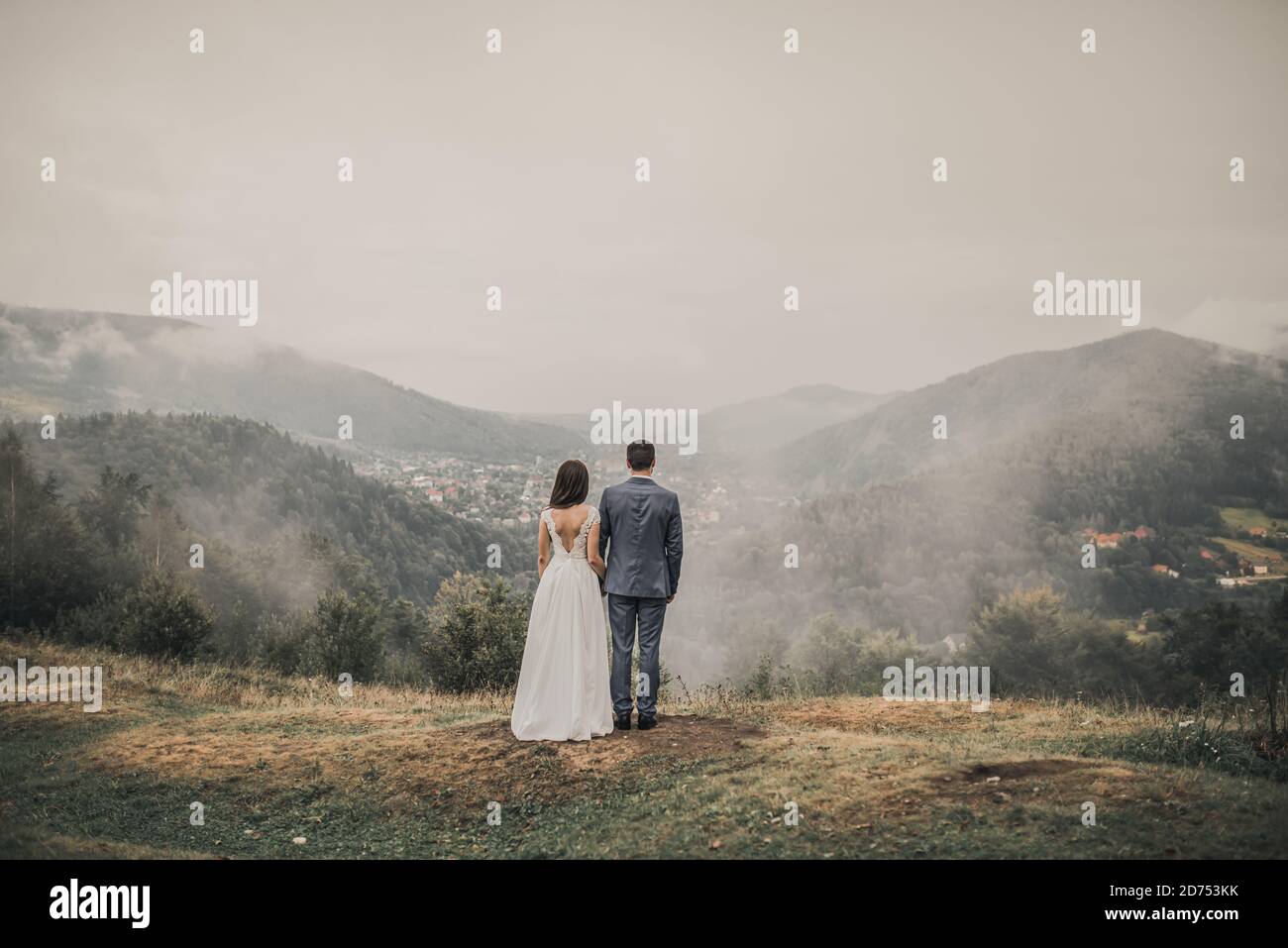 Braut steht mit dem Rücken mit dem Bräutigam am Berge im Nebel Stockfoto