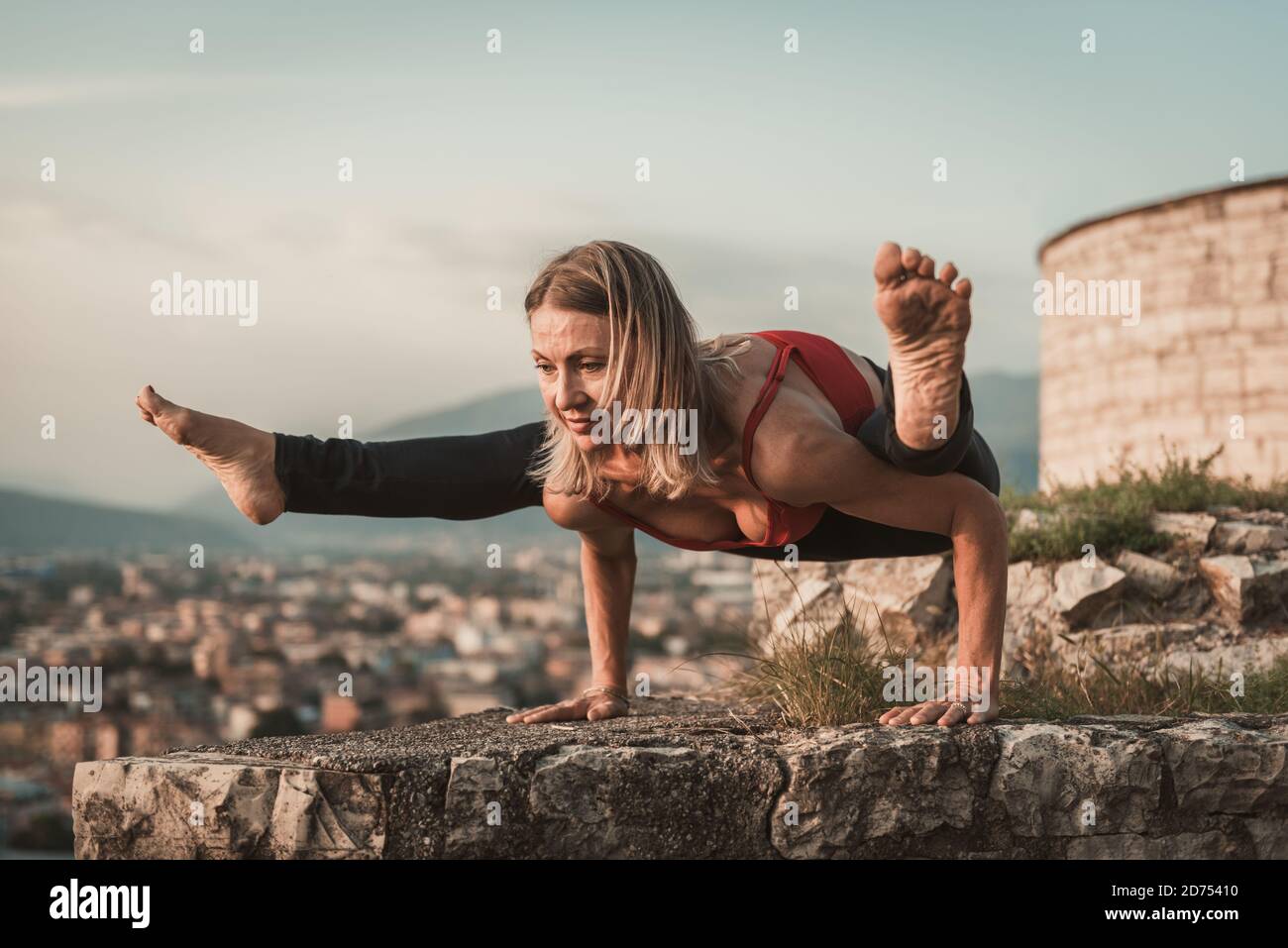 Erwachsene Frau macht Sport. Yogalehrer macht ein Asana an der alten Stadtmauer. Stockfoto