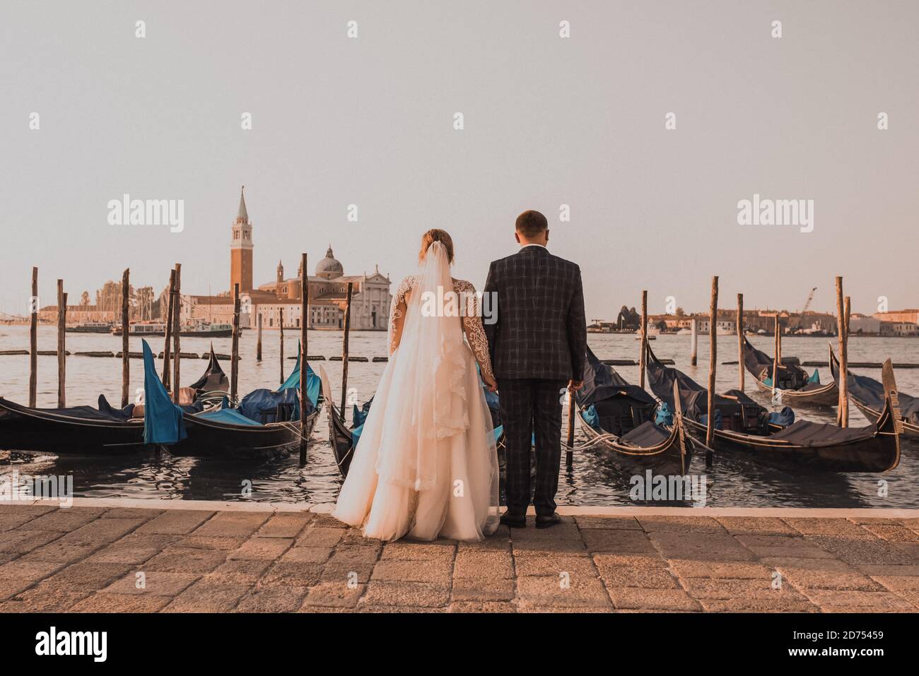 Ein Hochzeitspaar steht auf dem Pier in Venedig. Boote schwimmen auf dem Wasser Stockfoto