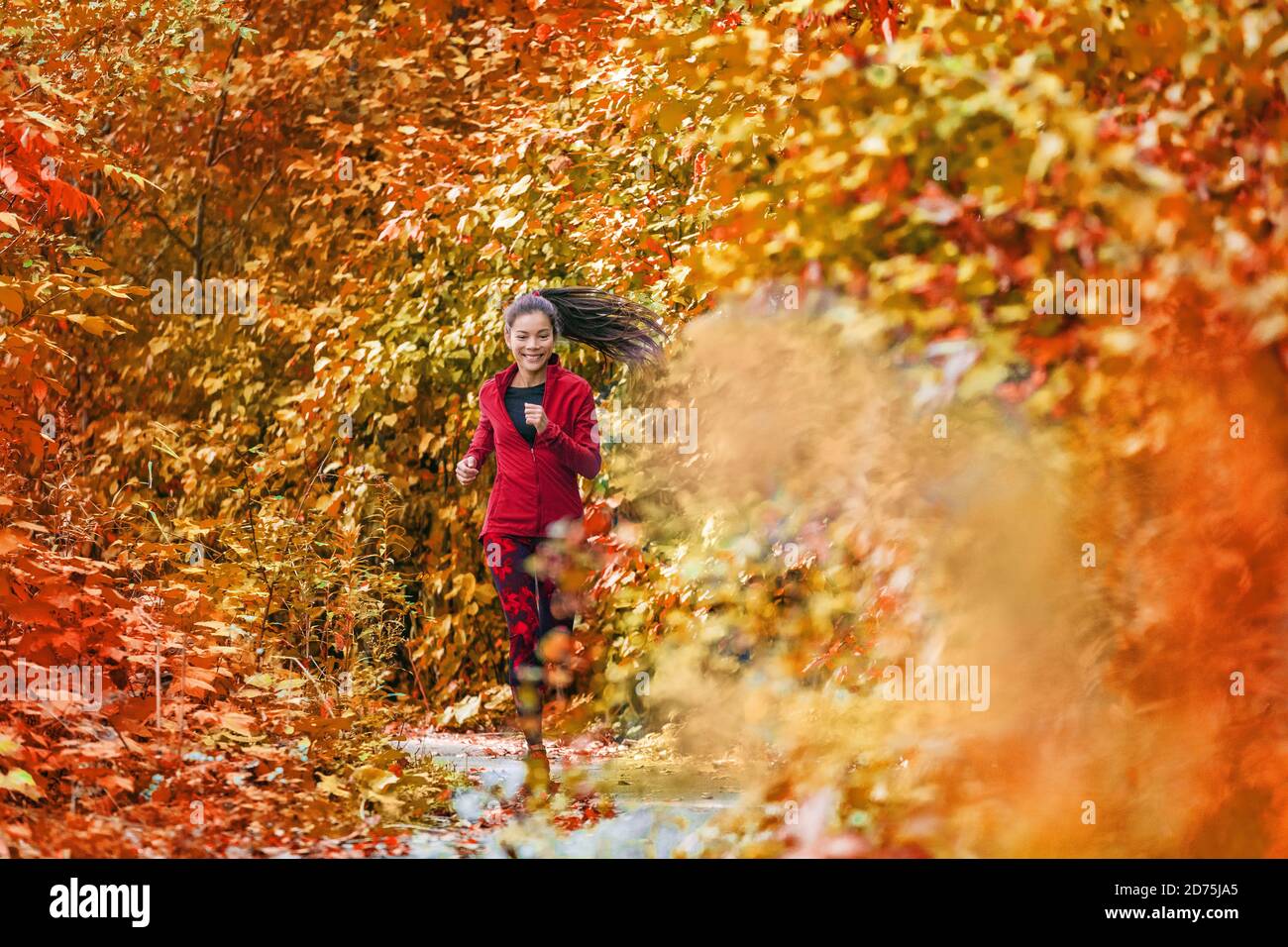 Herbst Laub Läufer Frau läuft in Wald Wälder mit schönen Farben in Baum Blätter Natur Hintergrund. Trail Run Athlet asiatische Mädchen glücklich Stockfoto