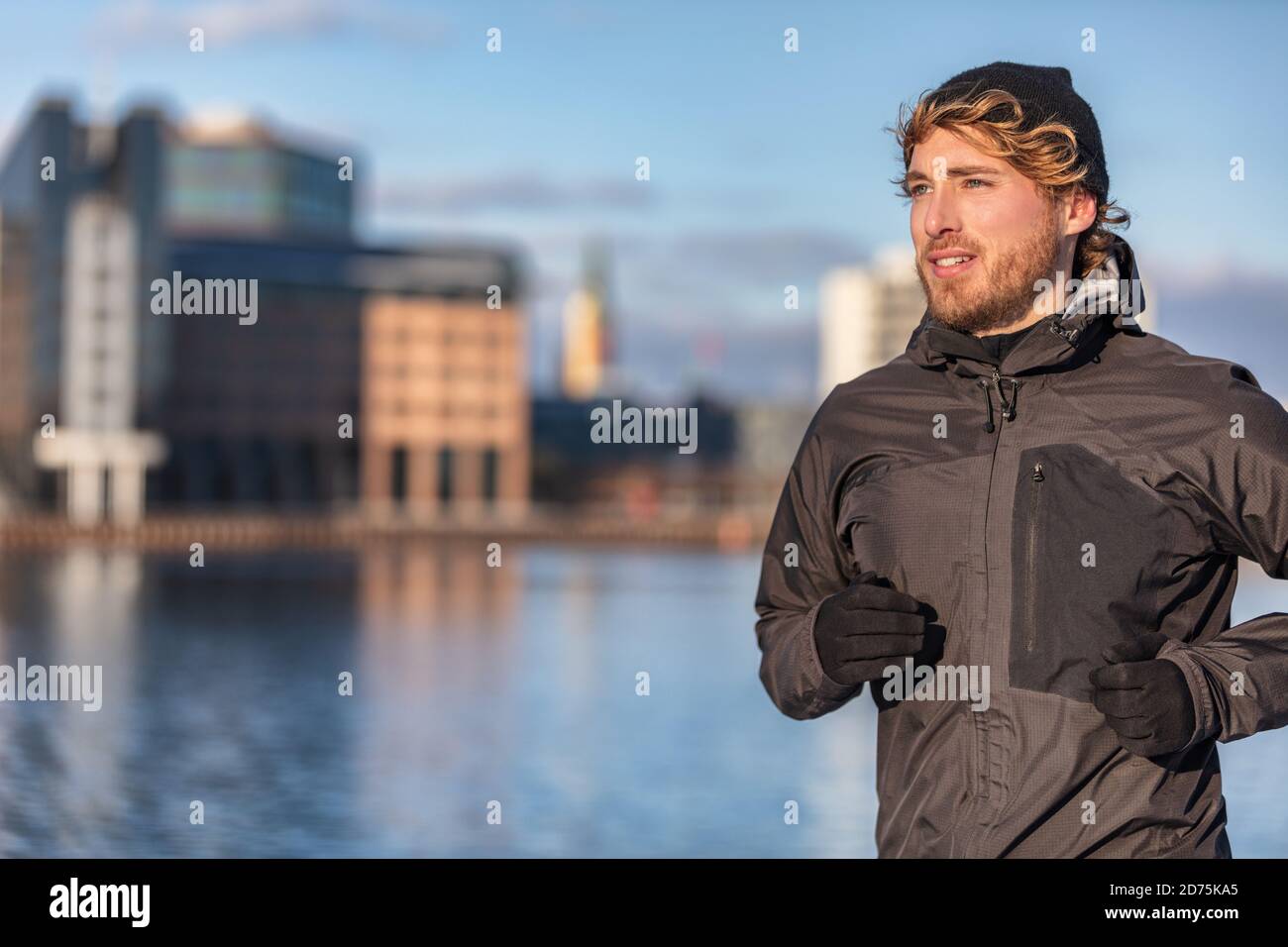 Winter laufen Sportler Mann joggen im Freien in der Stadt außerhalb tragen kaltes Wetter Zubehör - Hut, Handschuhe, winddichte Sportjacke. Aktiv gesund Stockfoto