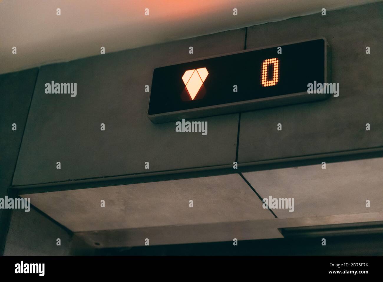 Bildschirm für die Bodenanzeige des Aufzugs. Monitor zeigt orange Nummer Null Boden und Pfeil nach unten im Aufzug. Stockfoto