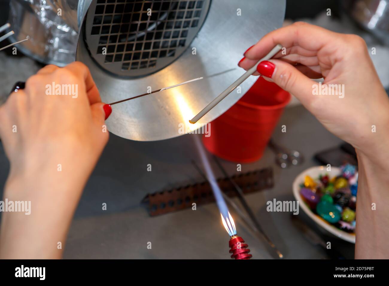 Der Künstler erhitzt das Glas mit einem Gasbrenner. Der Prozess der Herstellung von Glasschmuck. Die Hände des Meisters aus der Nähe Stockfoto