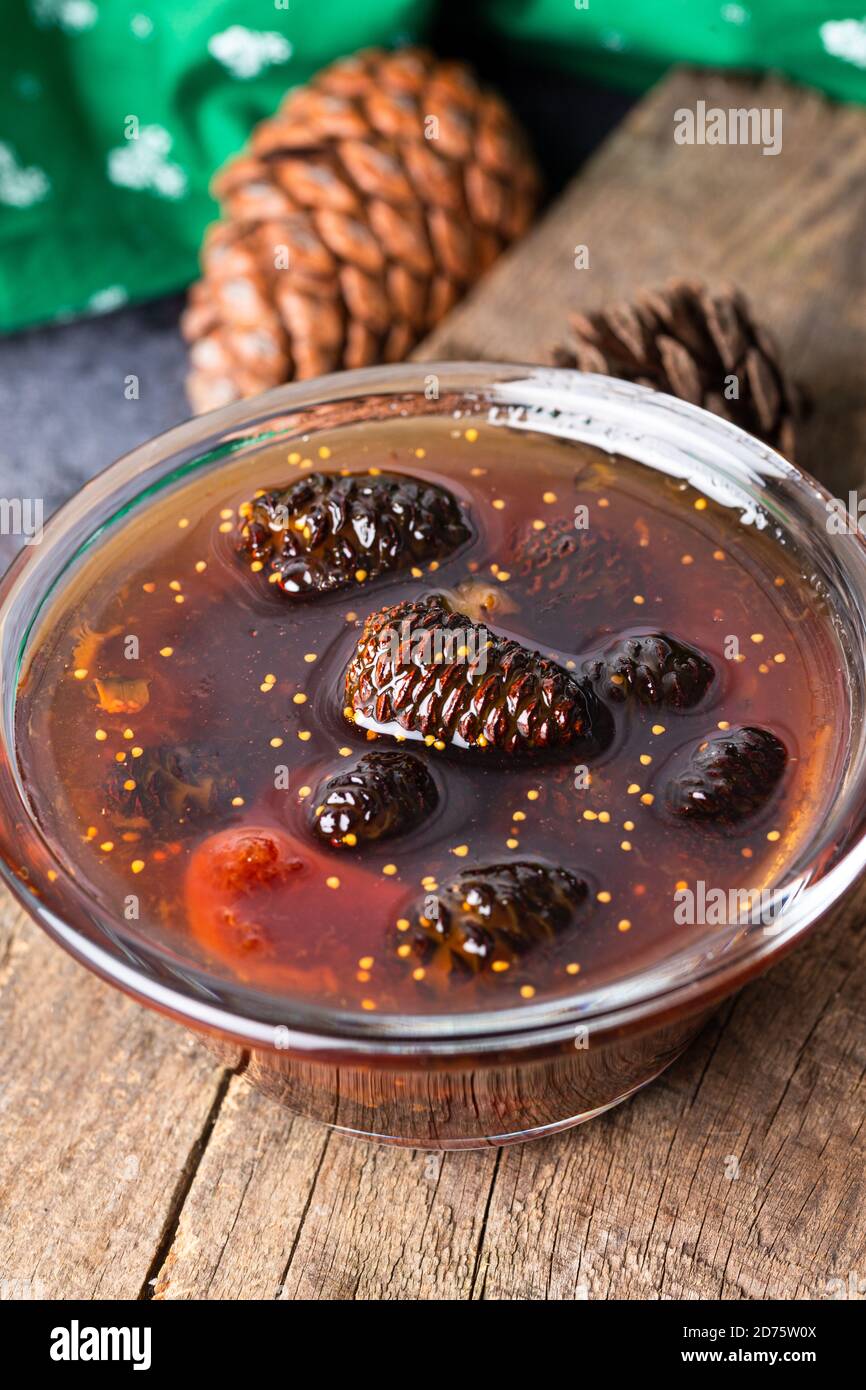 Junge Tannenzapfen verklemmen sich in einer Glasschale auf einem Holzbrett. Leckere Marmelade mit den kleinen Pinienzapfen. Stockfoto