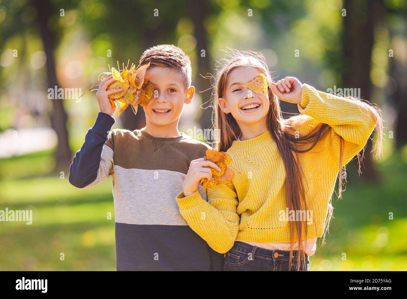 Glückliche Zwillinge Jugendliche Junge und Mädchen posiert umarmt sich im Herbst Park mit gefallenen gelben Blättern in der Hand bei sonnigem Wetter. Herbstthema Stockfoto