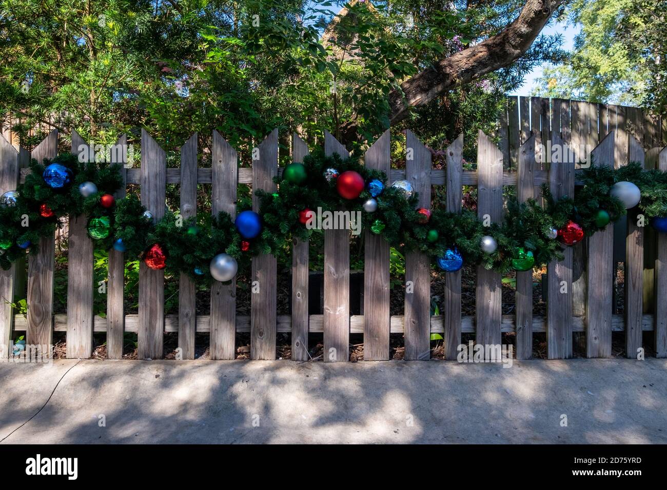 Ein heller strukturierter Holzzaun mit einer Weihnachtsgirlande, die in der Mitte der Barriere entlang geloopt ist. Stockfoto