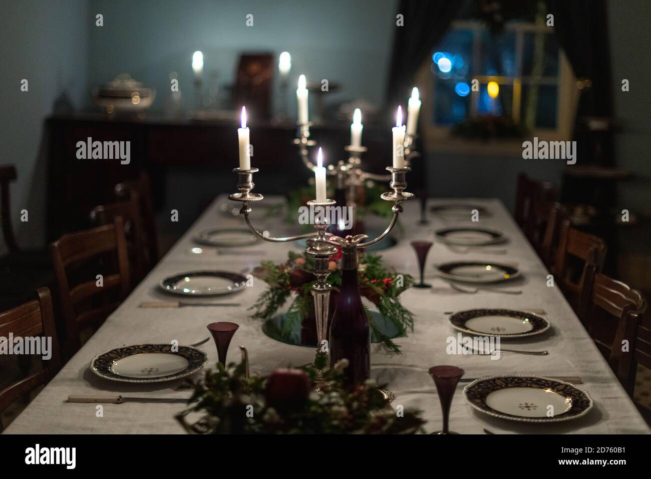 Ein dunkler romantischer formeller Esstisch mit Vintage-porzellan-Tellern, silbernen Kerzenleuchtern mit weiß beleuchteten Kerzen, einer weißen Tischdecke, floral Stockfoto