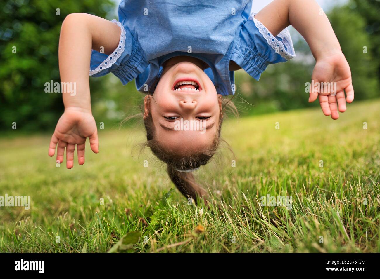 Lustige glückliche kleine Mädchen auf dem Kopf auf dem Gras im Park stehen. Stockfoto