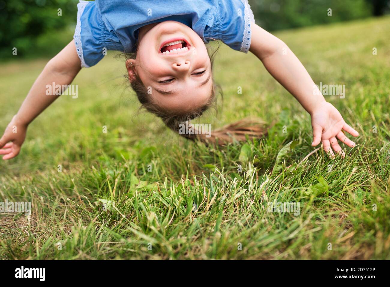 Lustige glückliche kleine Mädchen auf dem Kopf auf dem Gras im Park stehen. Stockfoto