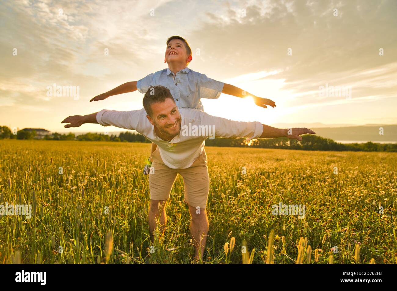 Die glückliche Familie des Vaters und des Kindes auf dem Feld bei der Sonnenuntergang Spaß auf dem Vater zurück Stockfoto