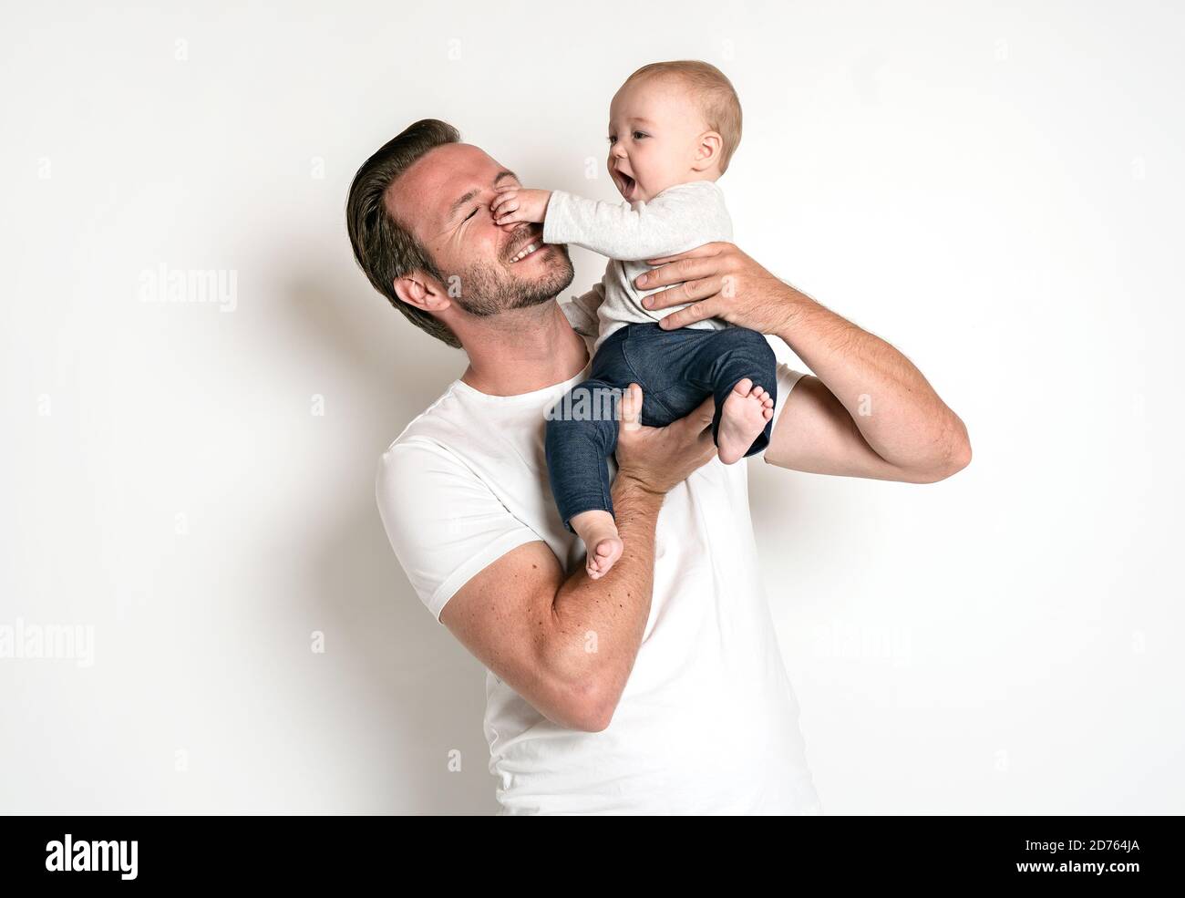 Mann hält ein lächelndes 6 Monate altes Baby, isoliert auf weiß. Das Baby hält die Nase des Vaters. Ziemlich komische Situation Stockfoto