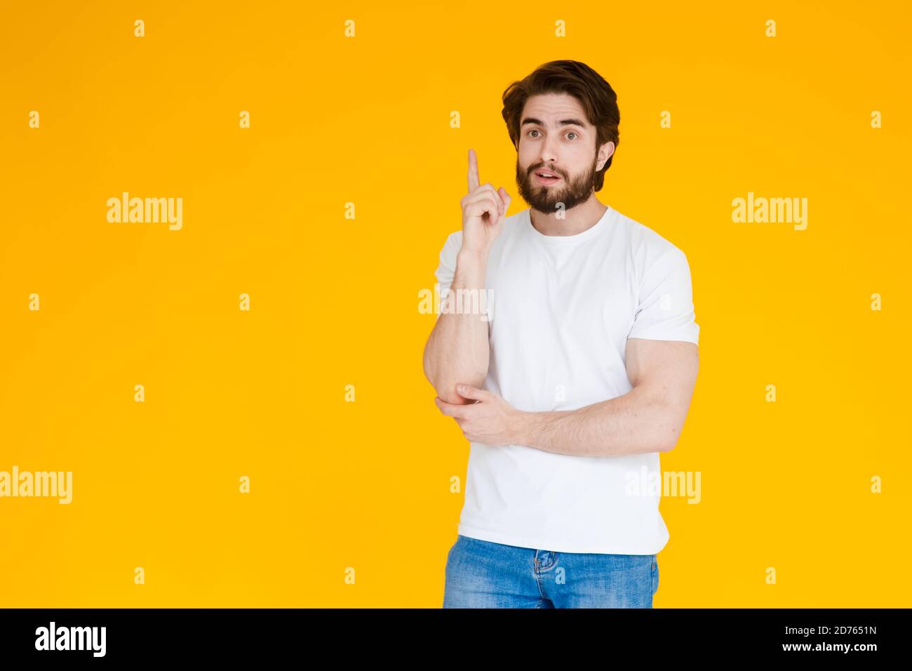 Junger hübscher Mann mit bartweißem Hemd, das über gelbem Hintergrund steht und mit dem Finger nach oben zeigt, mit einer erfolgreichen Idee. Begeistert und glücklich. Nummer eins. Stockfoto