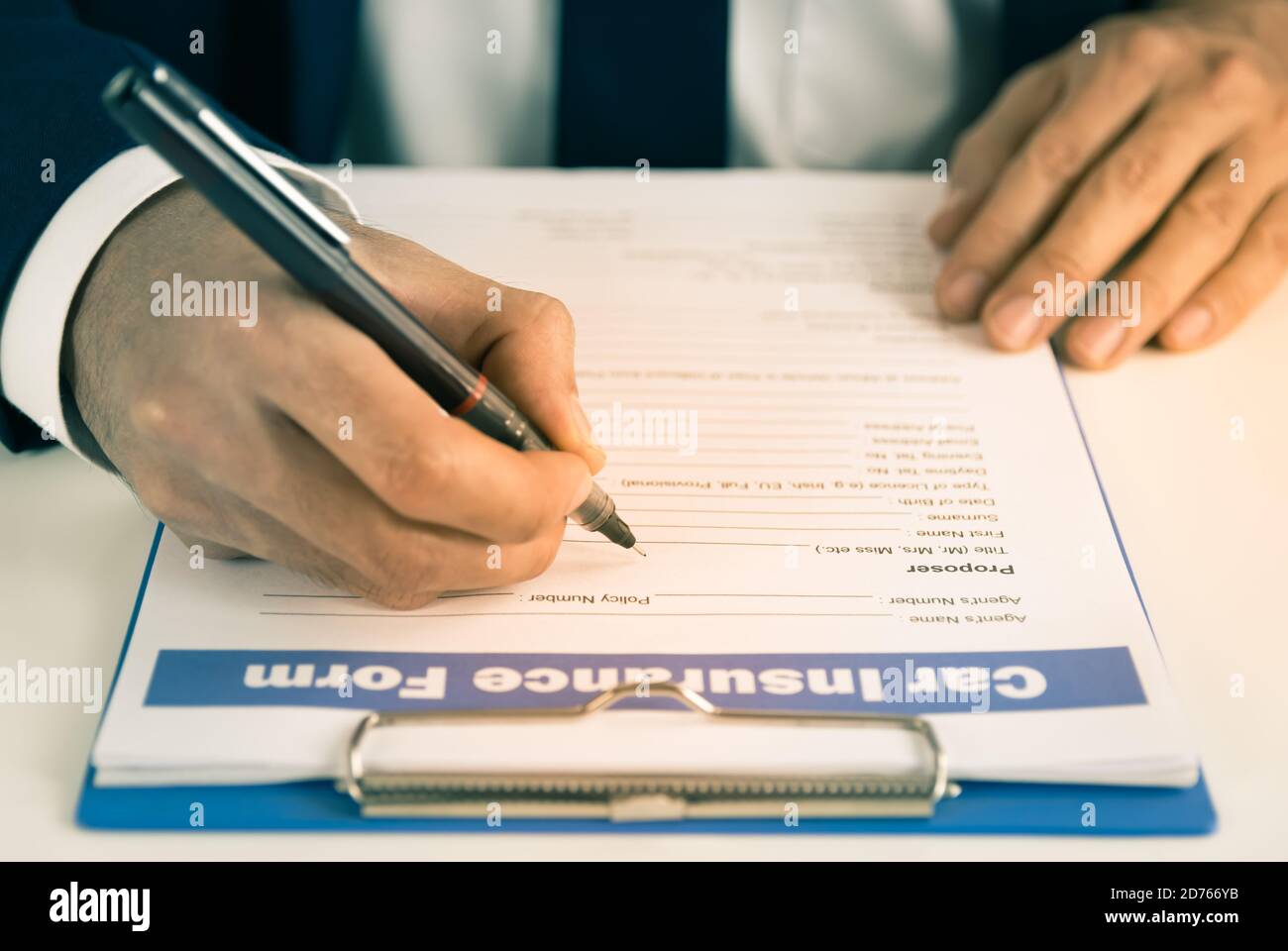 Zoom Versicherung Agent Hand Schreiben Auto Versicherung Anspruch Formular oder Versicherungsdokument auf Bürotisch im Vintage-Ton Stockfoto