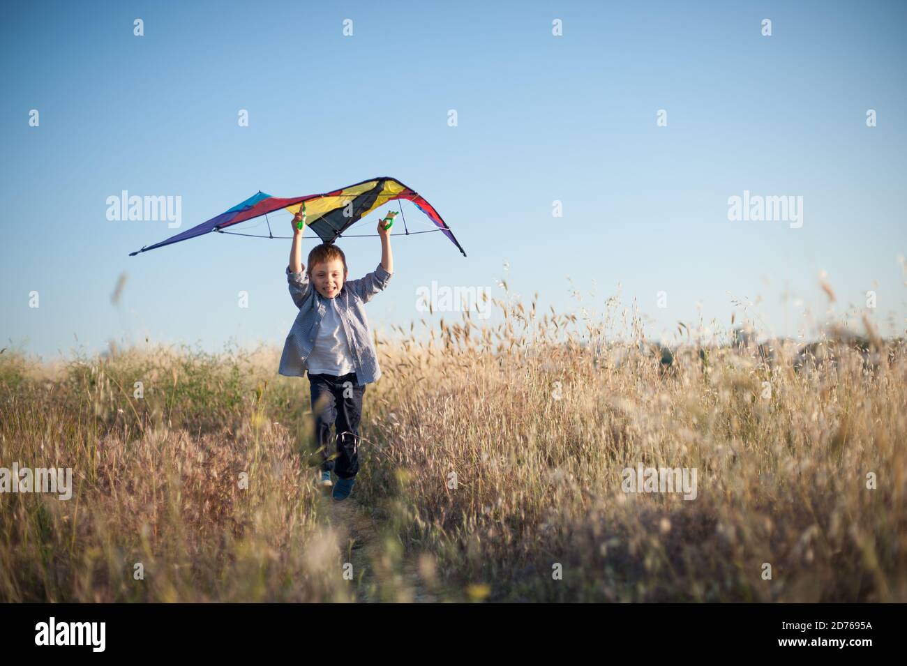 Aktiver kleiner Junge läuft mit Drachen über Kopf unter trockenen Grasfeld mit Kopierplatz Stockfoto