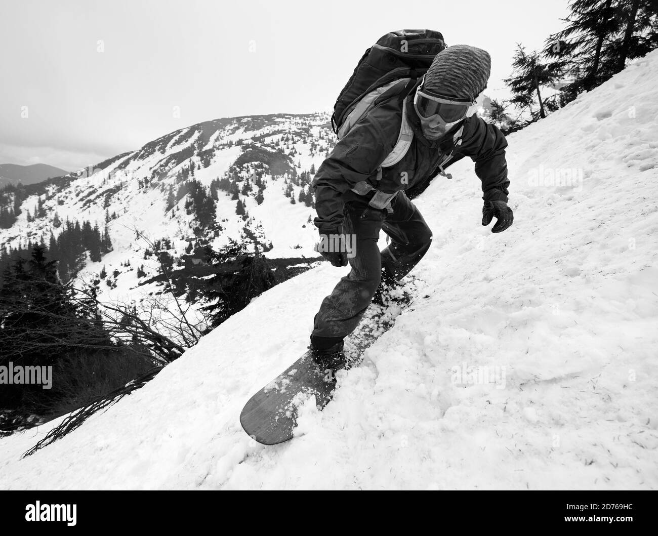 Junger Mann beim Snowboarden abseits der Piste auf einem steilen schneebedeckten Hochberg. Snowboarder in Brillen mit Rucksack in Aktion. Nahaufnahme vorne Stockfoto