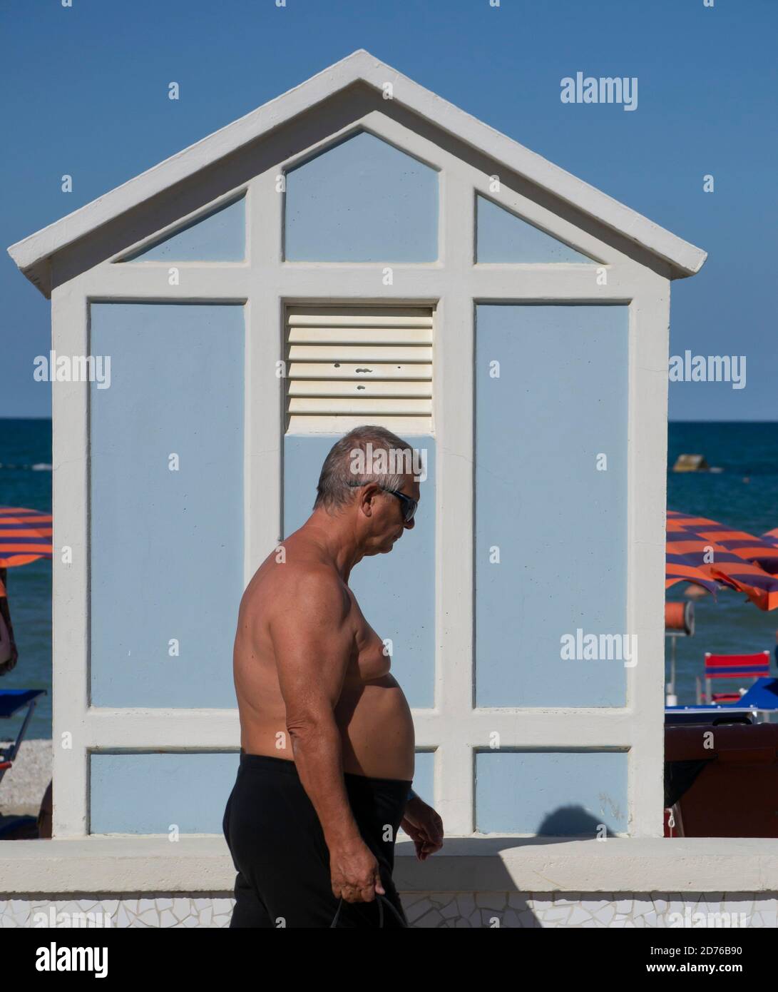 Ein Gentleman geht in Kostüm an der Küste von Marotta Vor einer Strandhütte Stockfoto