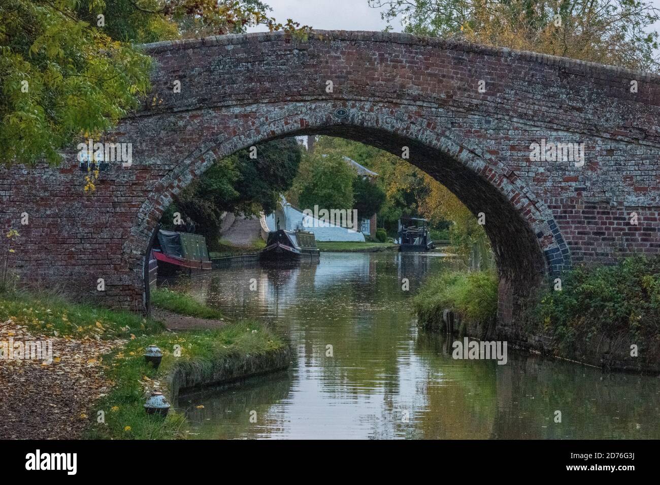 Brücke über den Grand Union Kanal mit Narrowbooten und Lastkähne, die entlang des Treidelpfades in Braunston, daventry, großbritannien, festgemacht sind Stockfoto