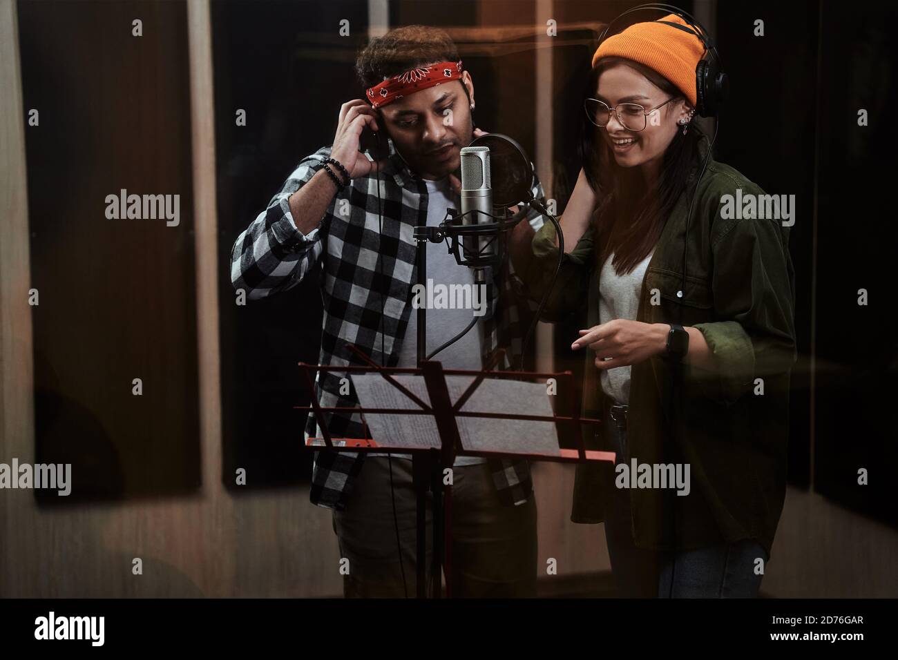 Porträt eines jungen Mannes und einer Frau, Duett, das Noten betrachtet, in einem Kondensatormikrofon singt, während er ein Lied in einem professionellen Studio aufnimmt Stockfoto