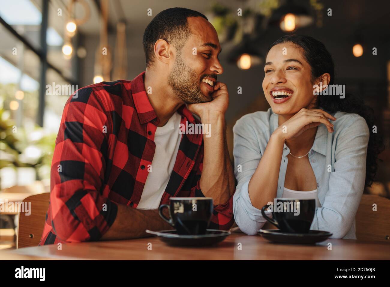 Schönes Paar, das zusammen im Café sitzt und lächelt. Mann und Frau sitzen auf Café-Tablet mit Tassen Kaffee. Stockfoto