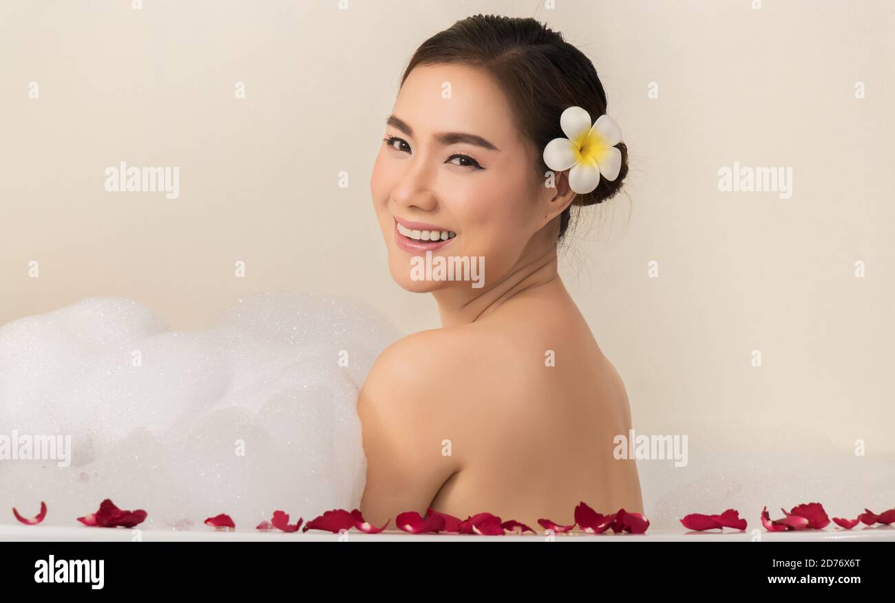 Entspannende schöne asiatische Frau Verwöhnung ihren Körper im Wasser in einer Spa-Badewanne mit weißem Schaum Seifenblase und Rosenblüten. Freizeitverfolgung Stockfoto