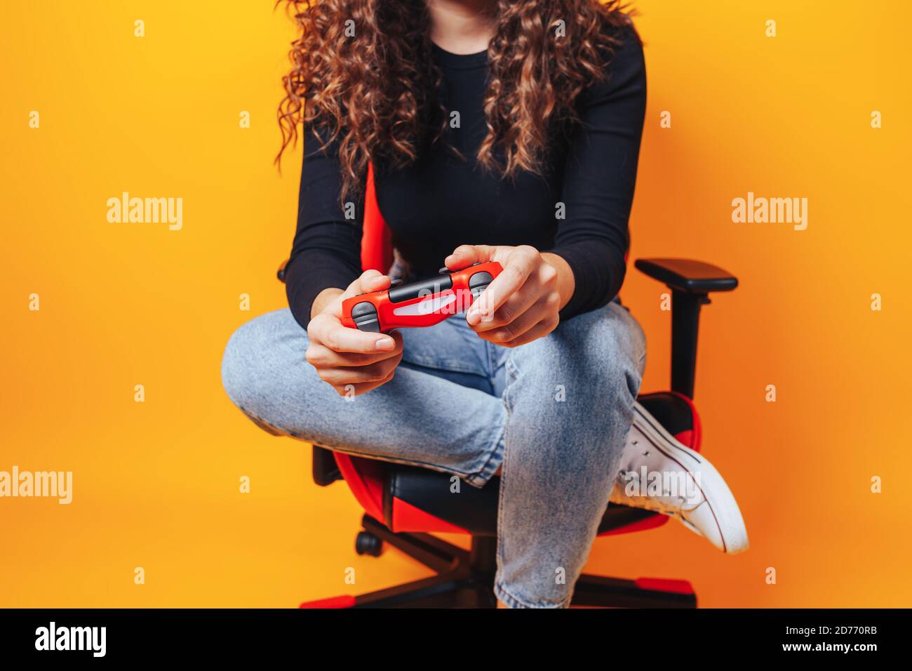 Frau, die hinter einem Spielstuhl in ihren Händen sitzt und rot hält Gamepad auf gelbem Hintergrund Stockfoto