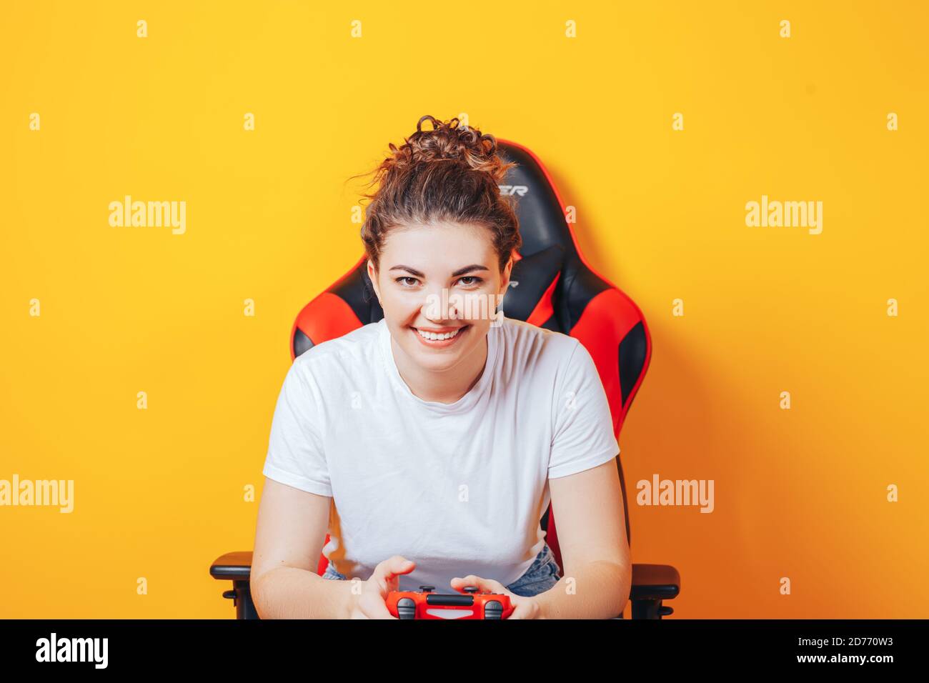 Frau, die hinter einem Spielstuhl in ihren Händen sitzt und rot hält Gamepad auf gelbem Hintergrund Stockfoto