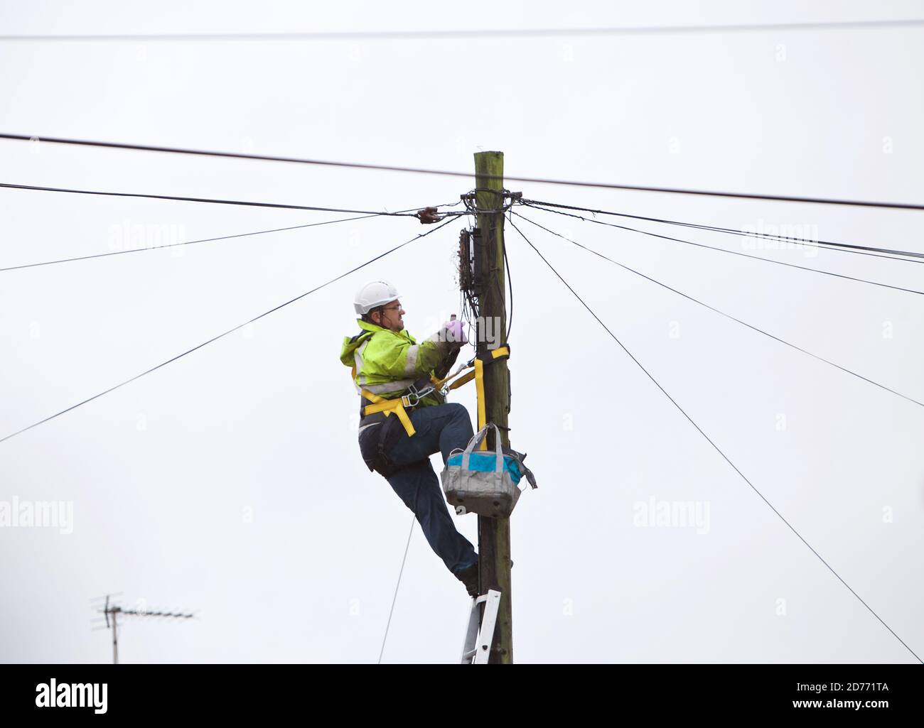 Ein offener Telekommunikationsingenieur bei der Arbeit auf einer Leiter trägt er die richtige PSA für die Arbeit in der Hand und erfüllt gleichzeitig die H&S-Vorschriften. Stockfoto