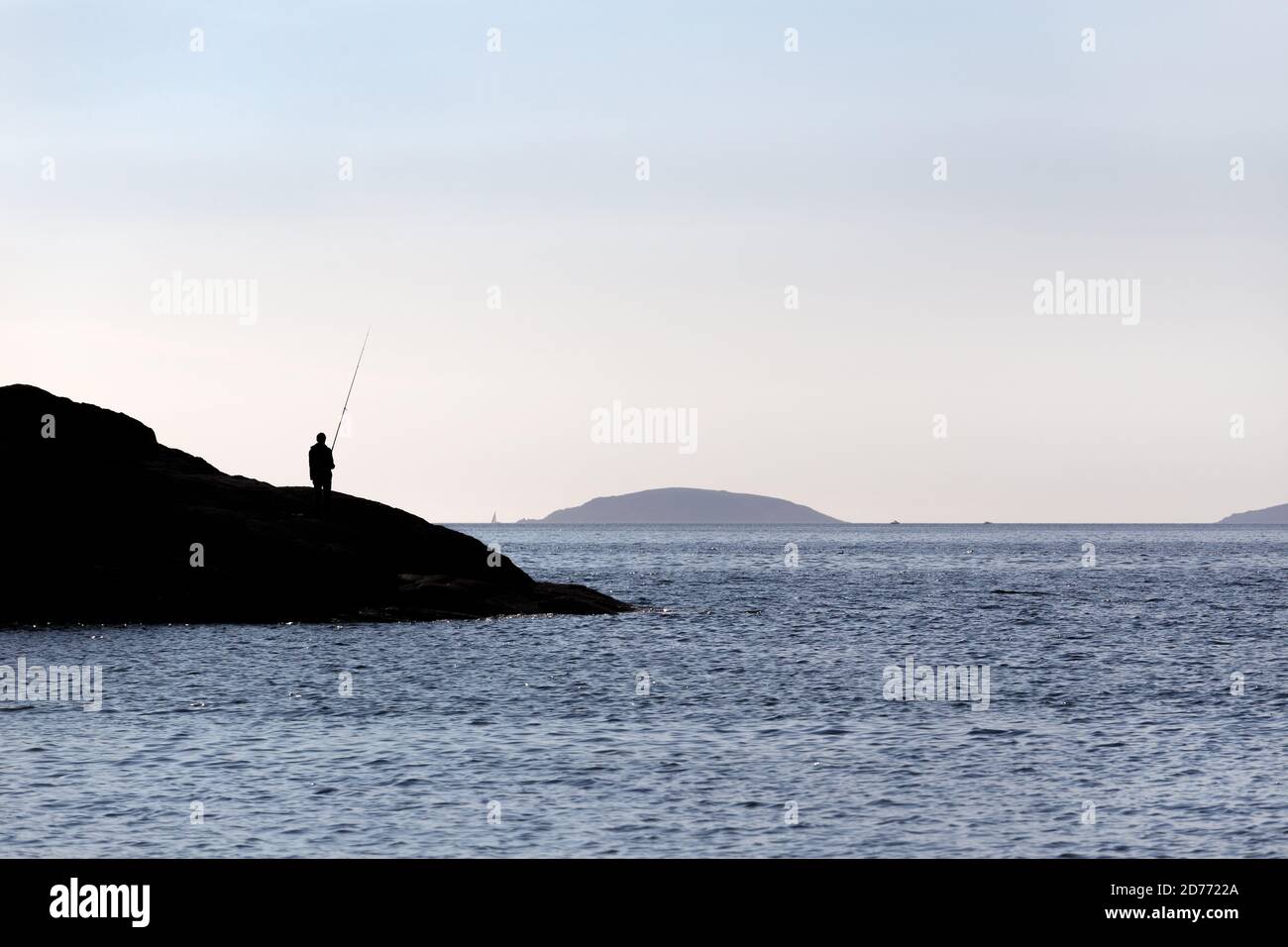 Silhouette eines Fischers auf Felsen mit Angelrute in der Nähe des Meeres an sonnigen Tag. Speicherplatz kopieren Stockfoto