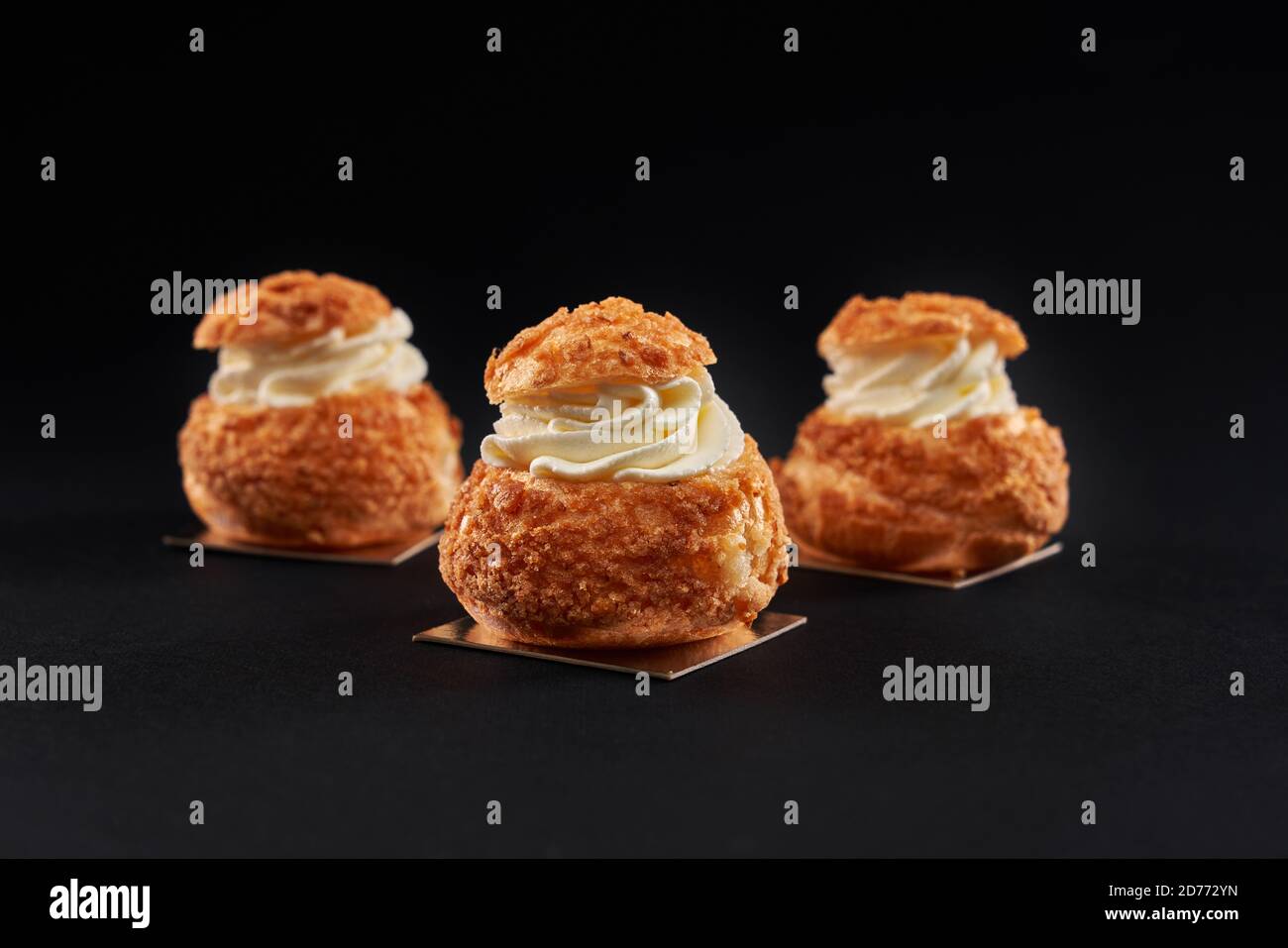 Nahaufnahme von Hree köstliche frische profiteroles mit süßen weißen Creme im Inneren. Hausgemachte leckere Eclare isoliert auf schwarzem Studio-Hintergrund. Konzept der Desserts, Restaurant Essen. Stockfoto