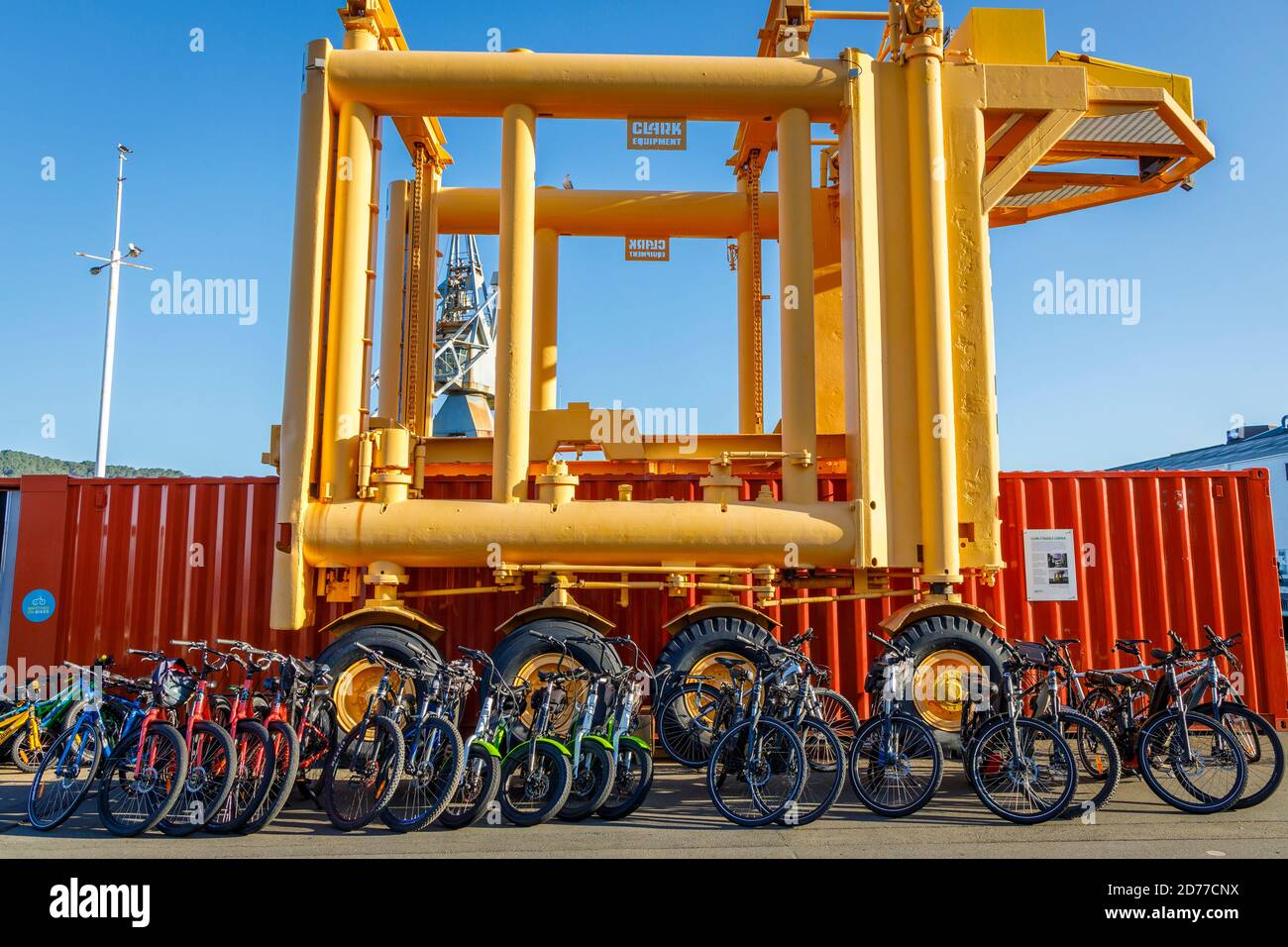 Ein Clark Straddle Carrier zum Bewegen von Containern. Hier mit Leihfahrrädern im Vordergrund. Queens Wharf, Wellington, Neuseeland. Stockfoto