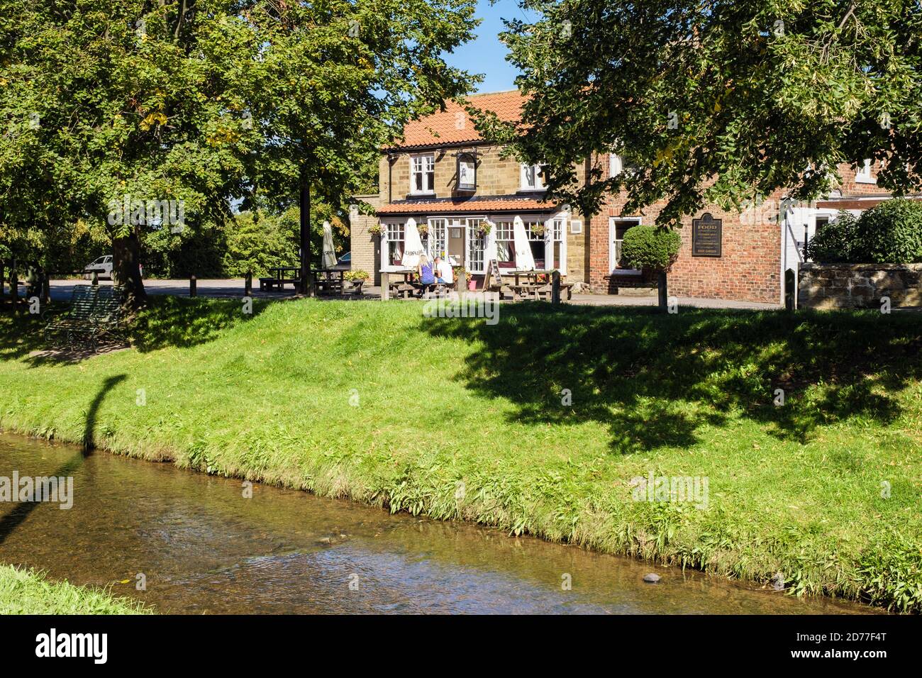 Kunden, die vor dem Black Horse Country Village Pub über den Scugdale Beck Stream sitzen. Swainby, North Yorkshire, England, Großbritannien Stockfoto