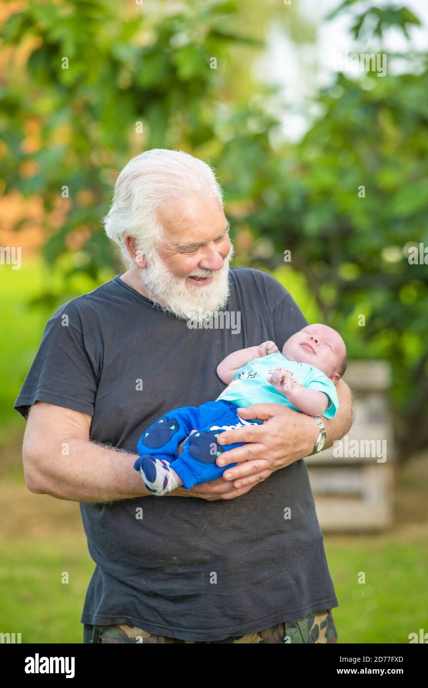 Ein älterer Bürger hält ein neugeborenes Baby in den Armen im Freien. Stockfoto