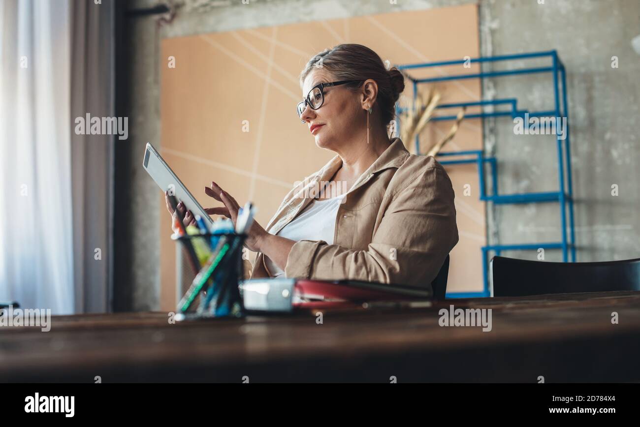Kaukasische ältere Frau mit Brille verwendet eine Tablette während Ein arbeitsreiches Tag von zu Hause aus Stockfoto