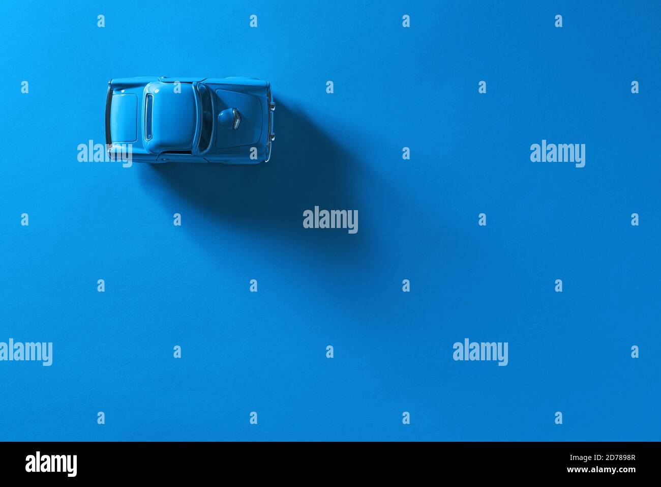 Draufsicht auf ein blaues Spielzeugauto auf blauem Hintergrund mit langem und seitlichem Schatten. Stockfoto