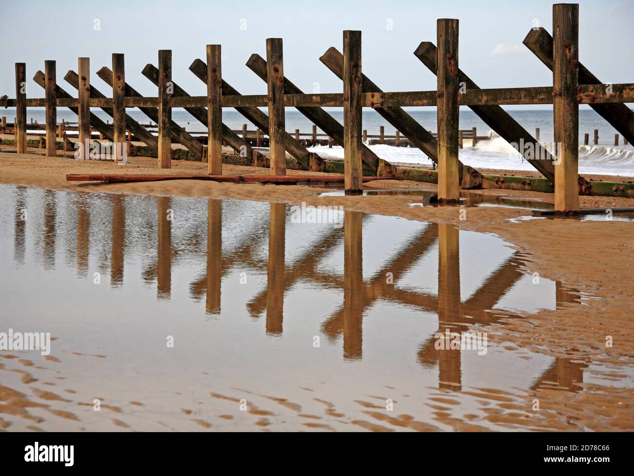 Ein verderbter Wellenbrecher mit fehlenden horizontalen Hölzern und Reflektion im Gezeitenbecken an der Nord-Norfolk-Küste in Happisburgh, Norfolk, England, Großbritannien. Stockfoto