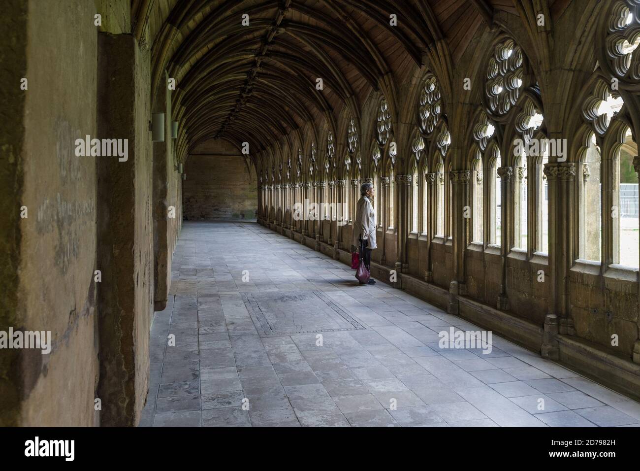 Ältere Frau schaut durch ein Fenster in den Cloisters, Lincoln Cathedral, Großbritannien; Konzept für Alter, einsam, verlassen. Stockfoto